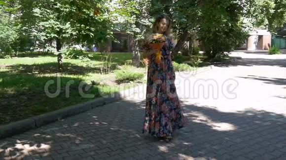 年轻的女人穿着一件漂亮的裙子走在公园里带着一束花视频的预览图