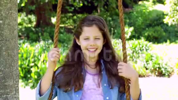 微笑的小女孩坐在公园的秋千上视频的预览图
