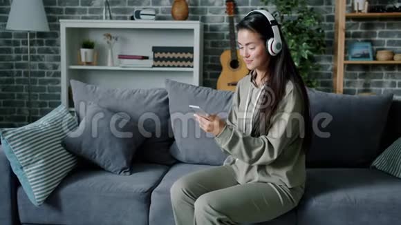 年轻女性在家里用耳机听音乐和使用智能手机视频的预览图
