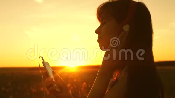 快乐的女孩听音乐在美丽的夕阳下跳舞戴着耳机和智能手机的年轻女孩视频的预览图