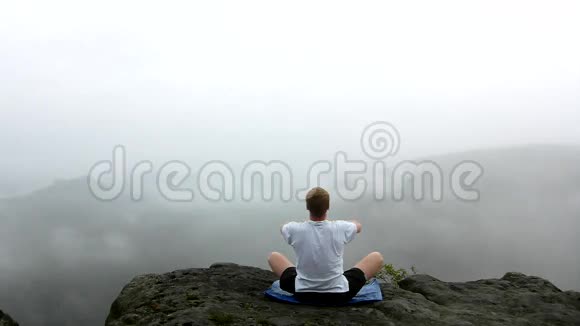 在雾蒙蒙的早晨人们在山顶上做瑜伽姿势视频的预览图