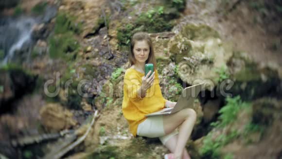有笔记本电脑的女孩坐在岩石上在森林里视频的预览图