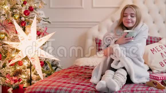 圣诞节室内的年轻女子坐着一个格子和一杯茶视频的预览图
