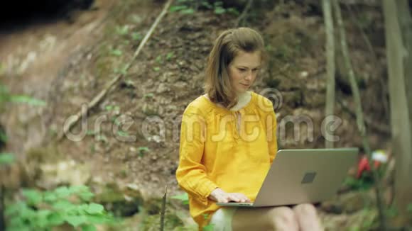 有笔记本电脑的女孩坐在岩石上在森林里视频的预览图
