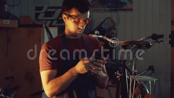 主题小企业自行车修复年轻的白种人黑发男子戴着安全护目镜手套使用移动电话视频的预览图