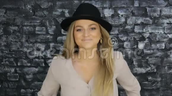 一个戴着黑帽子穿着灰色衬衫的女孩在砖墙背景下摆姿势视频的预览图