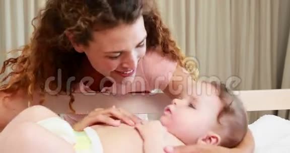 微笑着的母亲在婴儿床上玩婴儿视频的预览图