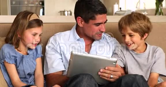可爱的孩子用平板电脑和父亲在沙发上视频的预览图