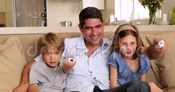 可爱的孩子们和他们的父亲在沙发上玩电子游戏视频的预览图