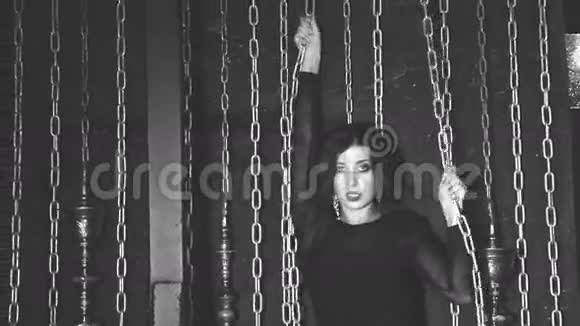 一个女孩在黑暗房间的锁链背景上的肖像黑白相间视频的预览图