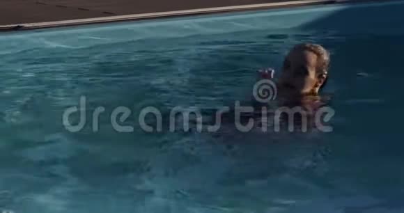 美丽的年轻女子穿着红色连衣裙在游泳池游泳化妆和口红视频的预览图