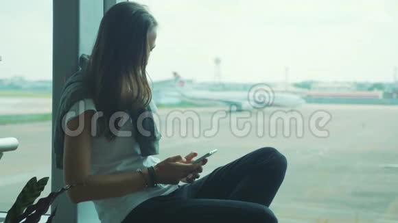 年轻女子在机场使用智能手机背景是飞机视频的预览图