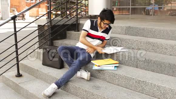 一位快乐的亚裔男学生坐在楼梯上看书的肖像视频的预览图
