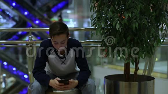 男孩坐在树旁的商店里用智能手机视频的预览图