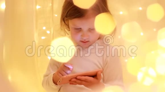 小女孩看着智能手机屏幕在下载的应用程序中播放视频的预览图