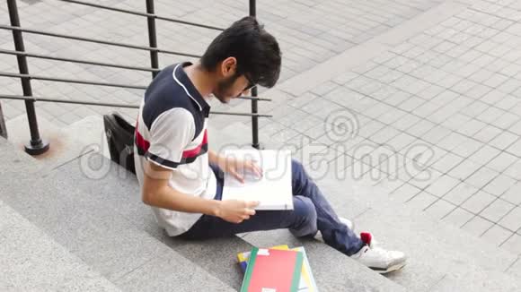 一位快乐的亚裔男学生坐在楼梯上看书的肖像视频的预览图