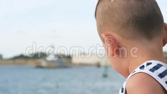 天空和大海背景上穿着水手条纹衬衫的滑稽小男孩视频的预览图
