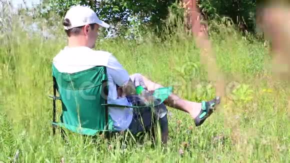 一个人坐在一片灯火通明的草地上的野餐椅上他休息然后离开草本植物和花朵从夏风中摇摆视频的预览图