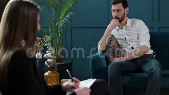 在蓝色办公室的心理治疗期间男性客户和女性心理学家坐在舒适的沙发上视频的预览图
