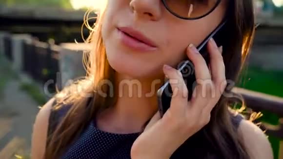 戴墨镜的女人在智能手机上说话在日落时分走在街上特写镜头视频的预览图