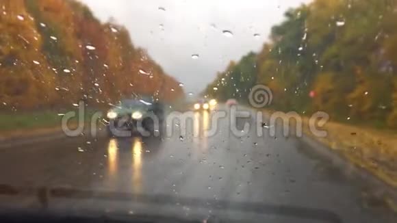 汽车在公路上行驶秋天美丽的风景林雨滴在玻璃车上模糊的背景缓慢视频的预览图