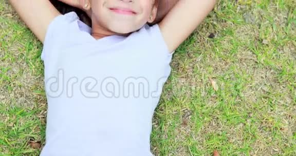 快乐的小女孩躺在草地上看着摄像机视频的预览图