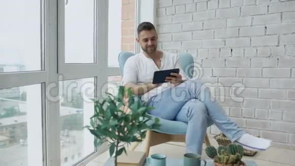 有魅力的男人在阁楼的阳台上坐着数码平板电脑视频的预览图