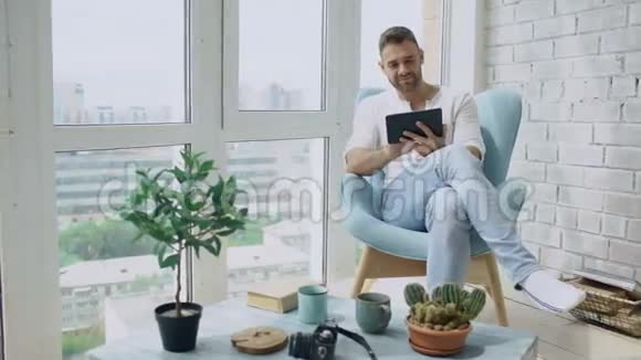 有魅力的男人在阁楼的阳台上坐着数码平板电脑视频的预览图