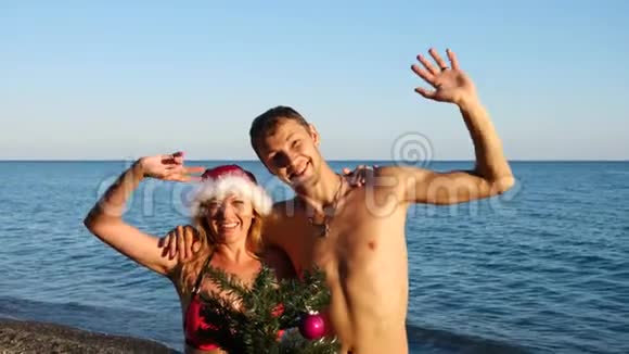 两个戴着圣诞帽的男人和女孩在海滩上迎接新年和圣诞节把圣诞树装饰在圣诞树上视频的预览图
