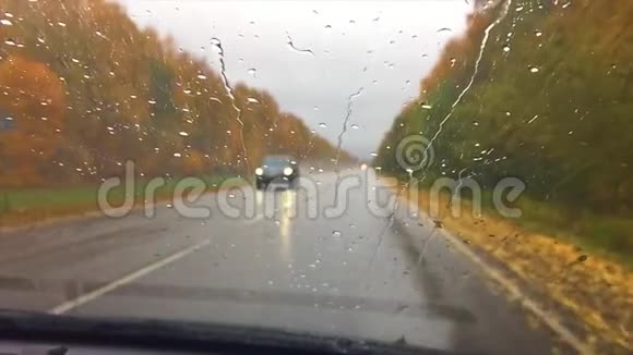 汽车行驶在路上秋天旅行美丽的风景林雨滴在玻璃车上行驶模糊的背景视频的预览图