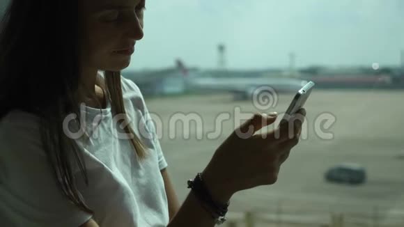 年轻女子在机场使用智能手机背景是飞机视频的预览图
