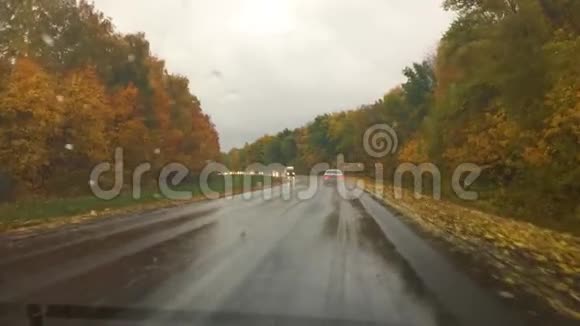 汽车行驶在路上秋天美丽的风景林雨滴在玻璃上的旅行车模糊的背景缓慢视频的预览图