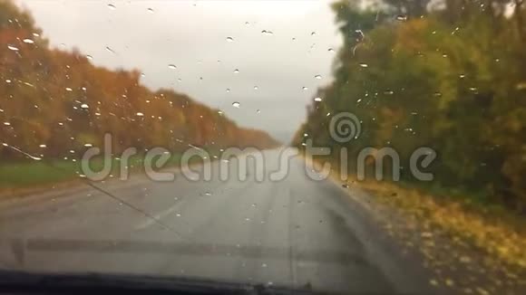 汽车上路沥青旅行秋天美丽的风景林雨滴在玻璃车上模糊的背景缓慢视频的预览图