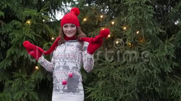 戴着红色围巾和手套的圣诞老人帽子的快乐的女人在圣诞树的背景下跳跃视频的预览图