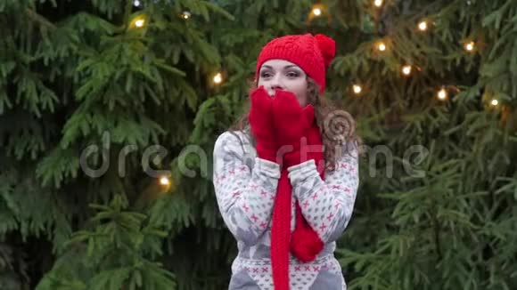 戴着红色围巾和手套的圣诞老人帽子的快乐的女人在圣诞树的背景下跳跃视频的预览图