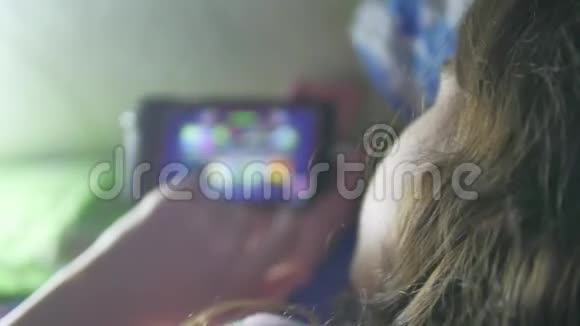 晚上躺在床上玩智能手机的快乐女孩视频的预览图