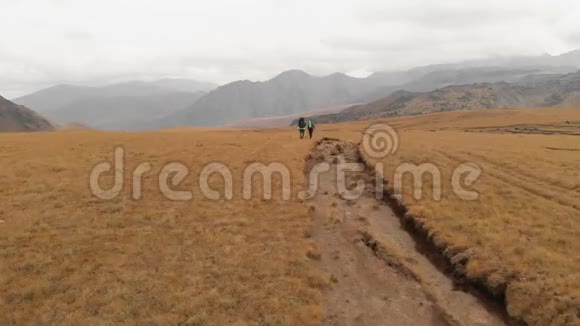 一对戴着帽子和太阳镜的大背包的旅行者男女在高山上漫步的鸟瞰图视频的预览图