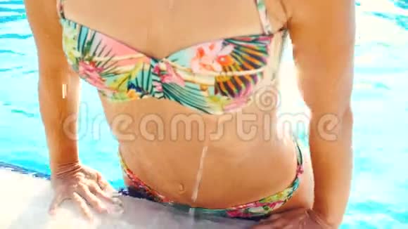 阳光明媚的夏日身着比基尼的年轻黑发女子在泳池里游泳视频的预览图