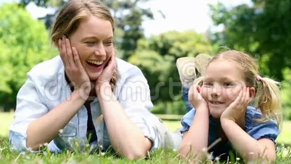 快乐的母亲和她的小女孩躺在草地上公园里视频的预览图