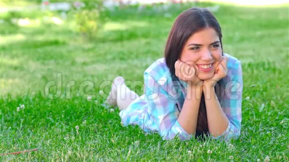 美丽的微笑女孩躺在户外的草地上视频的预览图