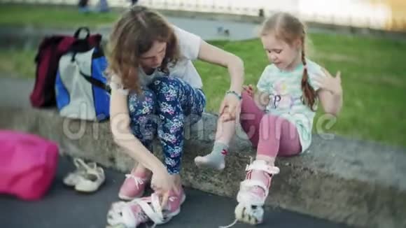 妈妈帮女儿戴上头盔和防护用具在公园里溜冰女人帮助女孩视频的预览图