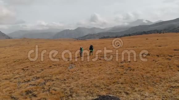 一对戴着帽子和太阳镜的大背包的旅行者男女在高山上漫步的鸟瞰图视频的预览图