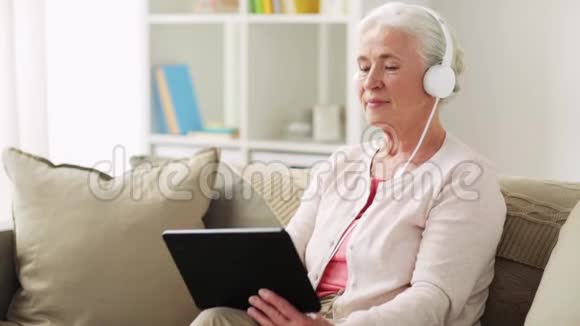 家里有平板电脑和耳机的老妇人视频的预览图