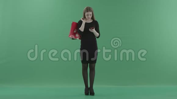 穿着小黑裙子的美女正在手机上发短信或上网手里拿着她的购物视频的预览图
