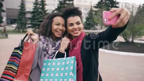 两个可爱的非裔美国女人带着购物袋和微笑自拍朋友们在参观商场销售后玩得很开心视频的预览图