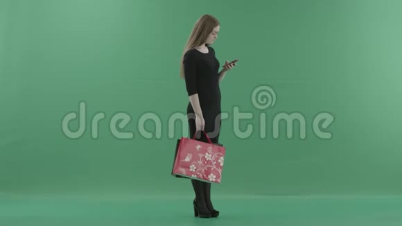 穿着小黑裙子的美女正在手机上发短信或上网手里拿着她的购物视频的预览图