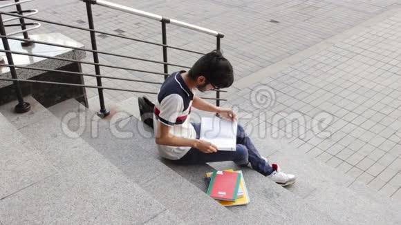 一位快乐的亚裔男学生坐在楼梯上每天看书的画像视频的预览图