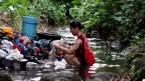 这个女人浸在膝盖的深水里甚至在污染的河流里洗衣服视频的预览图