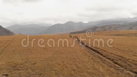 一对戴着帽子和太阳镜的大背包的旅行者男女在高山上漫步的鸟瞰图视频的预览图