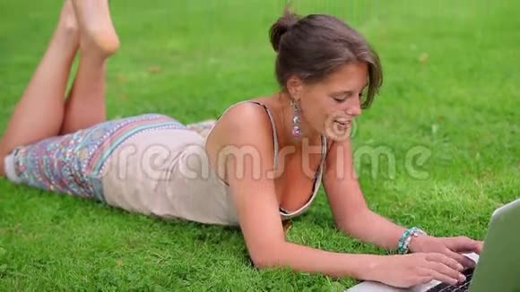 快乐的学生用她的笔记本电脑躺在草地上视频的预览图